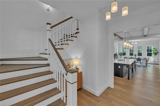 stairway with an inviting chandelier, hardwood / wood-style flooring, and beam ceiling