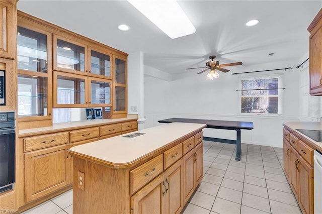 kitchen featuring light tile patterned flooring, dishwasher, a kitchen island, ceiling fan, and oven