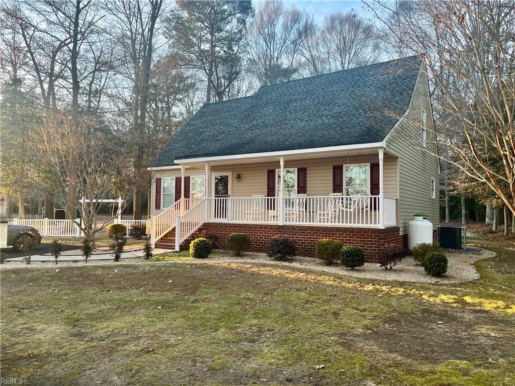 view of front of property featuring cooling unit, covered porch, and a front yard