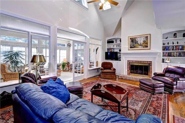 living room featuring built in features, ceiling fan, hardwood / wood-style floors, high vaulted ceiling, and a brick fireplace