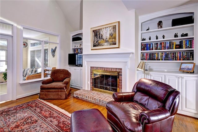 sitting room featuring a brick fireplace, lofted ceiling, light wood-type flooring, and built in shelves