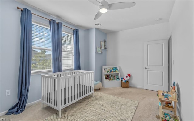 carpeted bedroom featuring a nursery area and ceiling fan