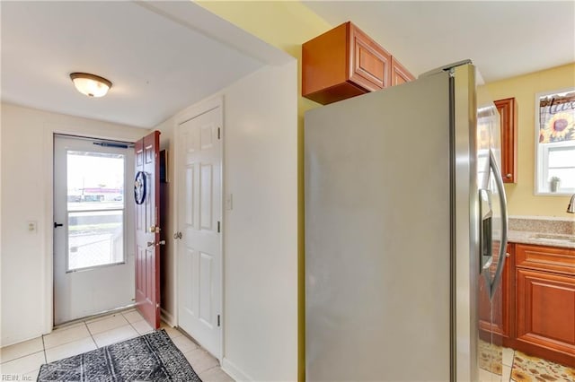 kitchen featuring stainless steel fridge, light stone countertops, sink, and light tile patterned floors