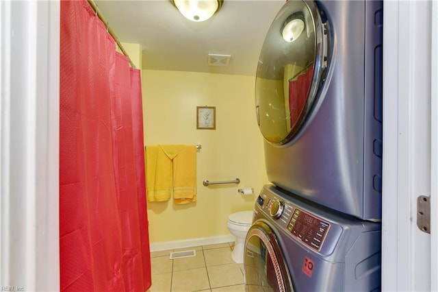 bathroom featuring tile patterned flooring, toilet, and stacked washer / dryer