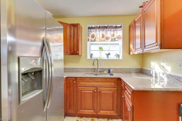 kitchen with sink, stainless steel fridge, and light stone countertops