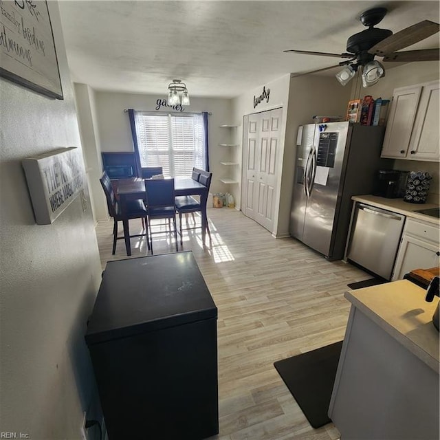 kitchen with white cabinetry, ceiling fan with notable chandelier, stainless steel appliances, and light hardwood / wood-style floors