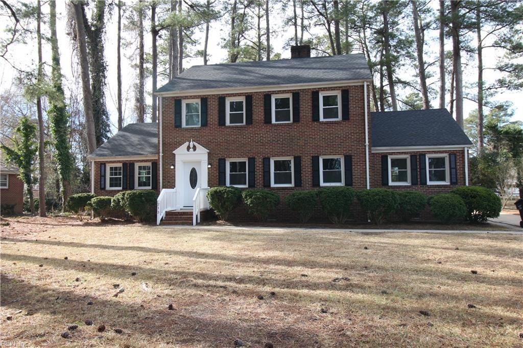 colonial home with a chimney, a front lawn, and brick siding