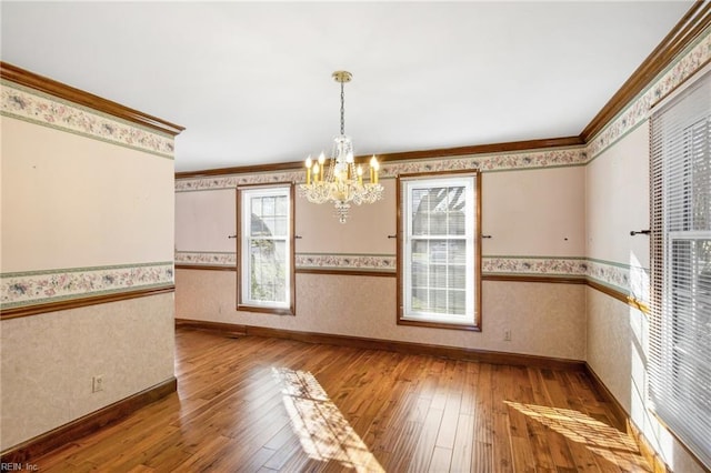 unfurnished dining area with hardwood / wood-style flooring, crown molding, and an inviting chandelier