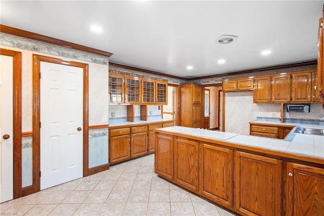 kitchen featuring light tile patterned flooring, tile countertops, kitchen peninsula, cooktop, and crown molding