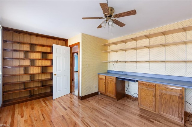 unfurnished office featuring ceiling fan, built in desk, and light hardwood / wood-style floors