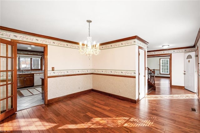 unfurnished dining area featuring sink, crown molding, wood-type flooring, and a chandelier