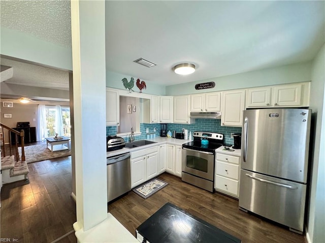 kitchen with appliances with stainless steel finishes, dark hardwood / wood-style floors, white cabinetry, sink, and decorative backsplash