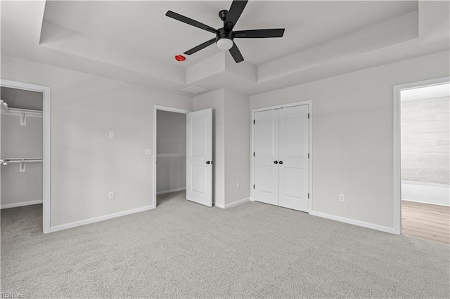 unfurnished bedroom with a raised ceiling, light carpet, and ceiling fan