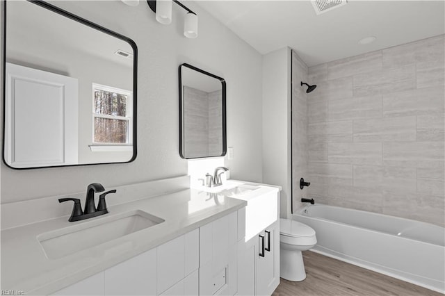 full bathroom with tiled shower / bath combo, vanity, hardwood / wood-style floors, and toilet