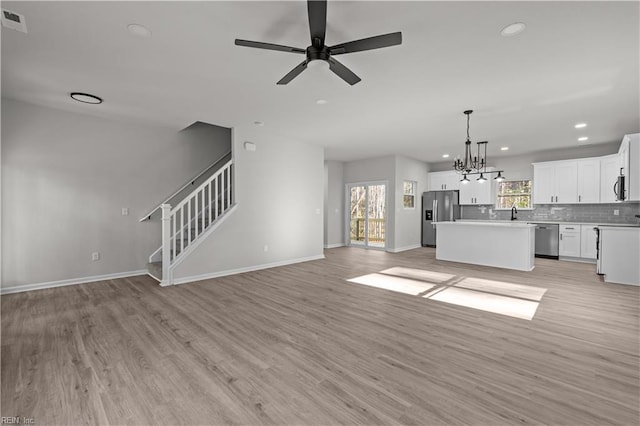 unfurnished living room featuring ceiling fan with notable chandelier and light hardwood / wood-style floors