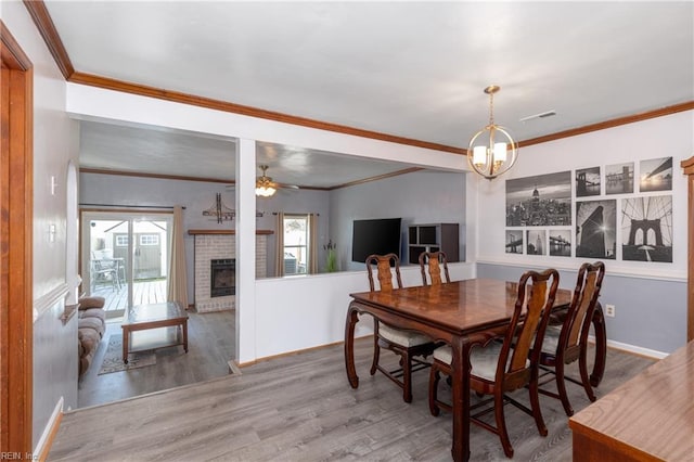 dining space with wood-type flooring, plenty of natural light, crown molding, and a brick fireplace