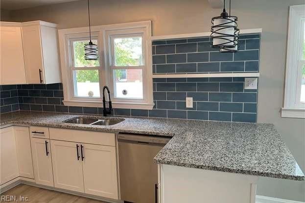 kitchen with tasteful backsplash, sink, white cabinets, hanging light fixtures, and stainless steel dishwasher