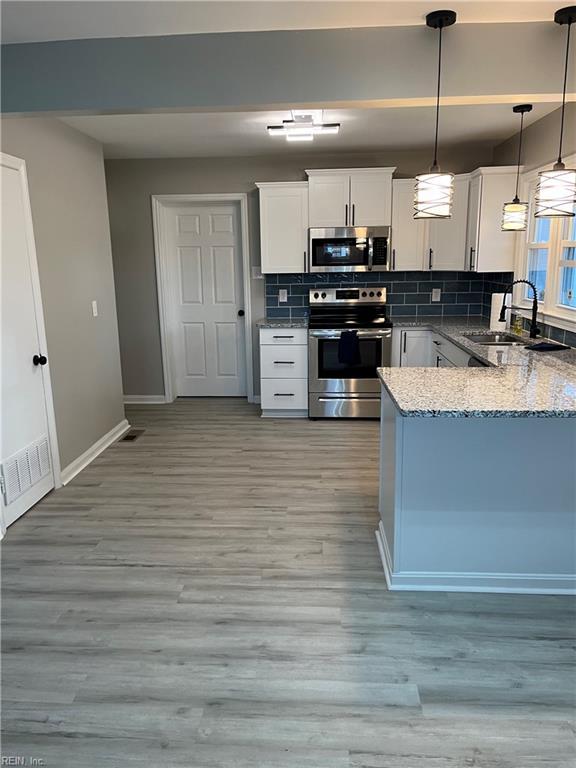 kitchen featuring tasteful backsplash, white cabinetry, sink, hanging light fixtures, and stainless steel appliances