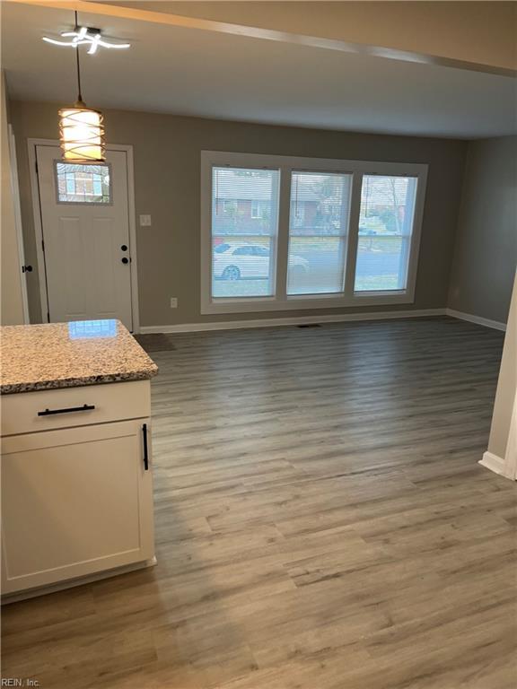 interior space with white cabinetry, light stone countertops, wood-type flooring, and pendant lighting