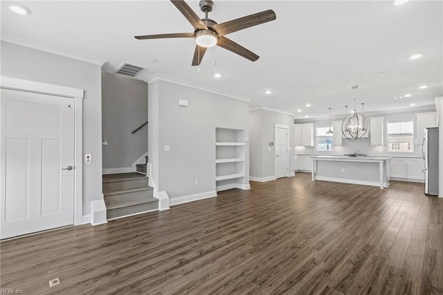 unfurnished living room featuring sink, crown molding, dark hardwood / wood-style floors, built in shelves, and ceiling fan with notable chandelier