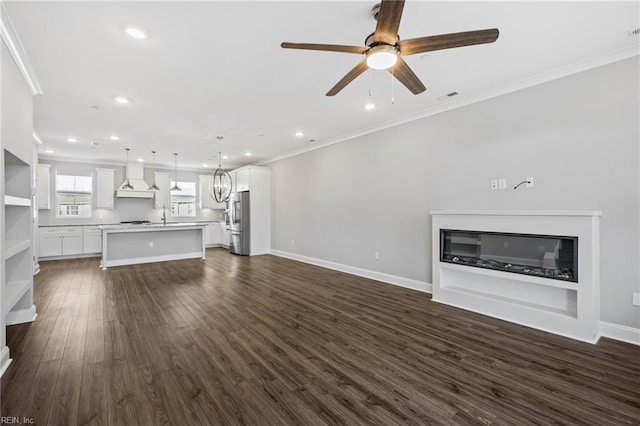 unfurnished living room featuring dark hardwood / wood-style flooring, sink, ornamental molding, and ceiling fan