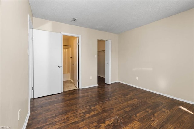 unfurnished bedroom with ensuite bath, a walk in closet, dark wood-type flooring, a textured ceiling, and a closet