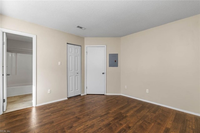 unfurnished bedroom with dark hardwood / wood-style floors, electric panel, a textured ceiling, and ensuite bath