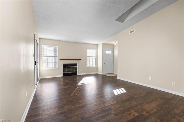 unfurnished living room with lofted ceiling, dark wood-type flooring, plenty of natural light, and a textured ceiling