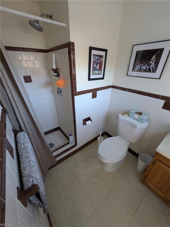 bathroom with a tile shower, vanity, tile walls, and toilet