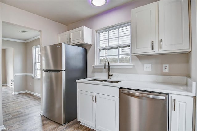 kitchen featuring sink, crown molding, appliances with stainless steel finishes, light hardwood / wood-style floors, and white cabinets