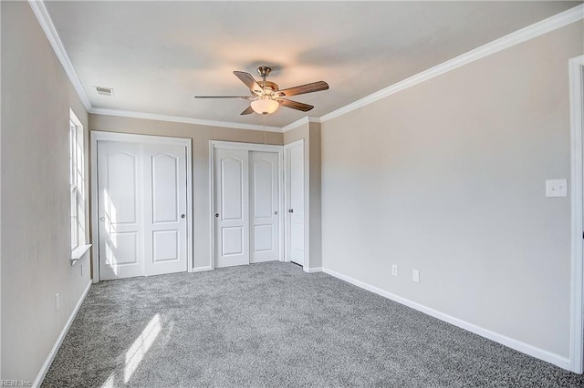 unfurnished bedroom with ceiling fan, ornamental molding, multiple closets, and carpet