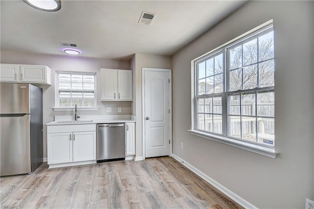 kitchen with appliances with stainless steel finishes, sink, white cabinets, and light hardwood / wood-style flooring