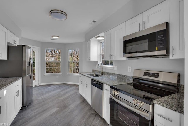 kitchen with stainless steel appliances, white cabinetry, sink, and dark stone countertops