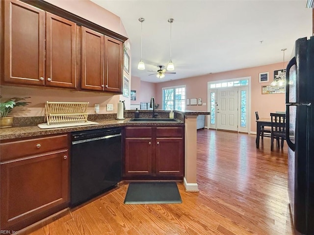 kitchen with sink, hanging light fixtures, black appliances, kitchen peninsula, and light wood-type flooring