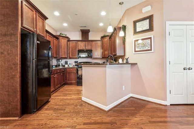 kitchen with pendant lighting, black appliances, sink, hardwood / wood-style flooring, and kitchen peninsula