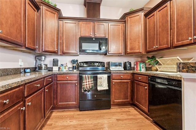 kitchen featuring dark stone counters, light hardwood / wood-style floors, and black appliances