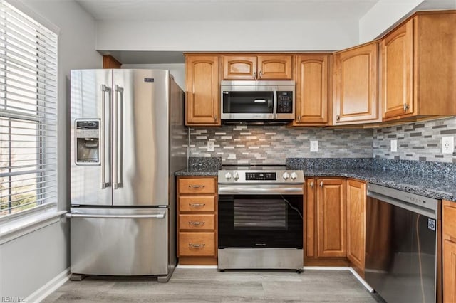 kitchen with stainless steel appliances, backsplash, light hardwood / wood-style floors, and dark stone counters