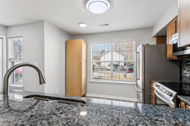 kitchen with stainless steel appliances, a wealth of natural light, sink, and dark stone countertops