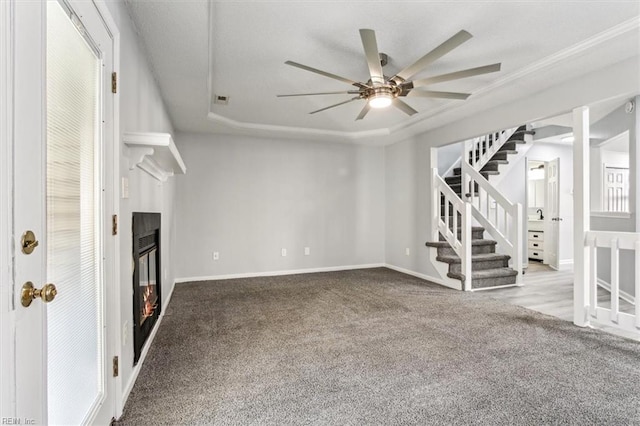 unfurnished living room with ceiling fan, light colored carpet, a large fireplace, and a raised ceiling