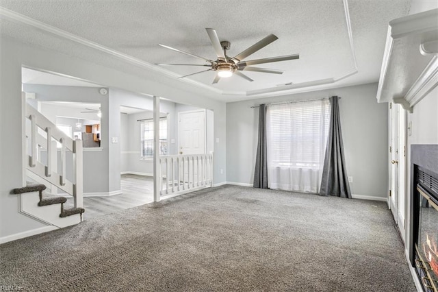 unfurnished living room with ceiling fan, light colored carpet, a textured ceiling, and a tray ceiling