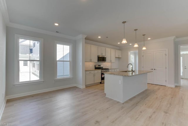 kitchen with sink, white cabinetry, appliances with stainless steel finishes, pendant lighting, and a kitchen island with sink