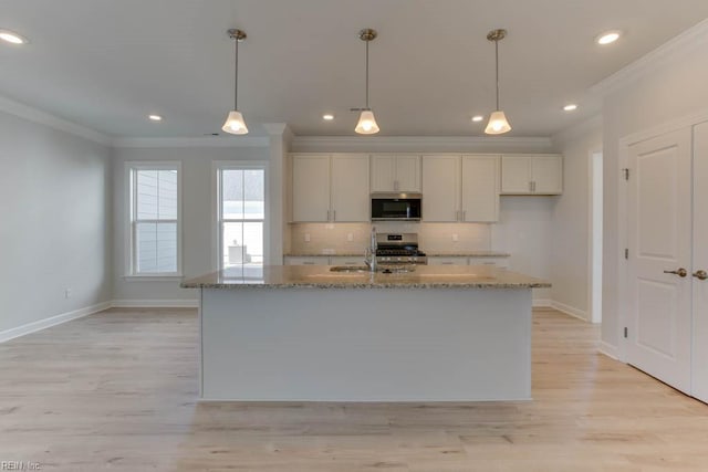 kitchen featuring white cabinetry, appliances with stainless steel finishes, light stone countertops, and an island with sink