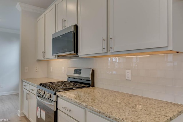 kitchen featuring white cabinetry, light stone counters, ornamental molding, appliances with stainless steel finishes, and decorative backsplash