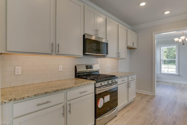 kitchen with crown molding, appliances with stainless steel finishes, backsplash, light stone counters, and a chandelier