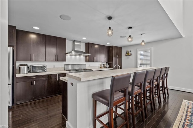 kitchen with pendant lighting, an island with sink, a kitchen breakfast bar, range, and wall chimney range hood