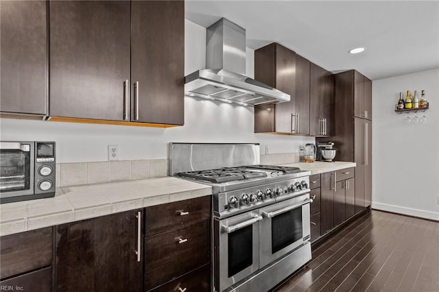 kitchen featuring range with two ovens, dark brown cabinets, dark hardwood / wood-style floors, and wall chimney exhaust hood