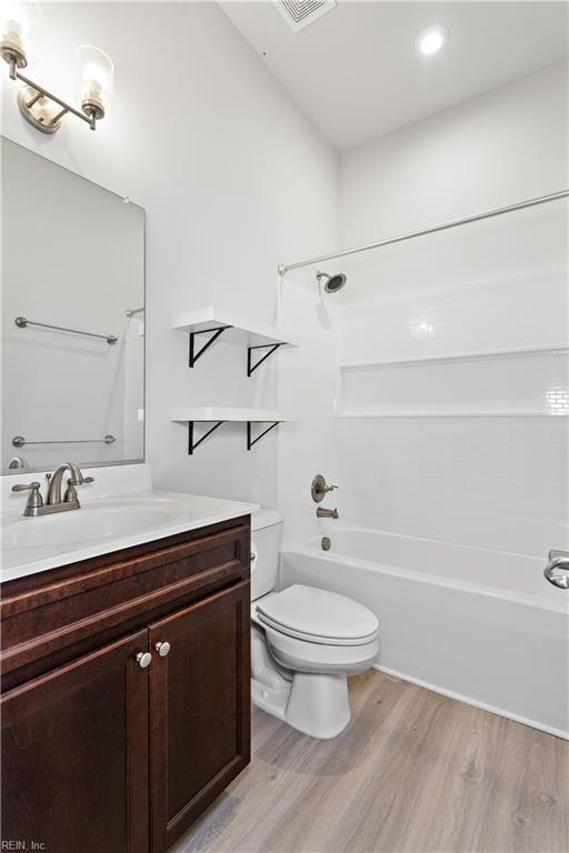 full bathroom with vanity, wood-type flooring, toilet, and washtub / shower combination