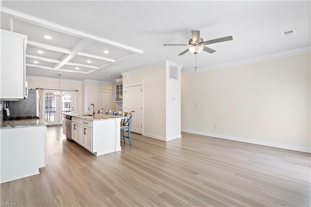 kitchen featuring pendant lighting, white cabinets, light stone counters, stainless steel appliances, and a center island with sink