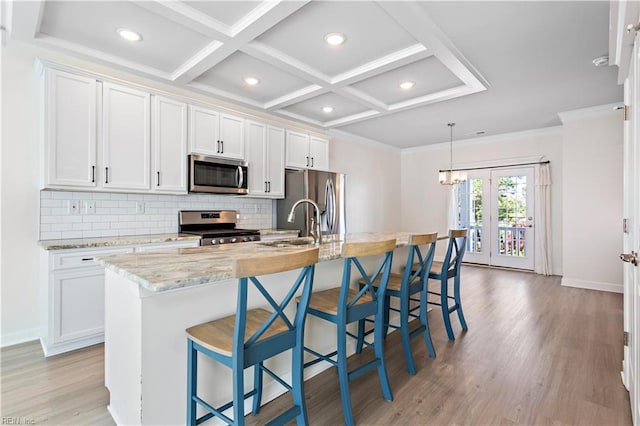 kitchen featuring white cabinetry, stainless steel appliances, light stone counters, and a center island with sink