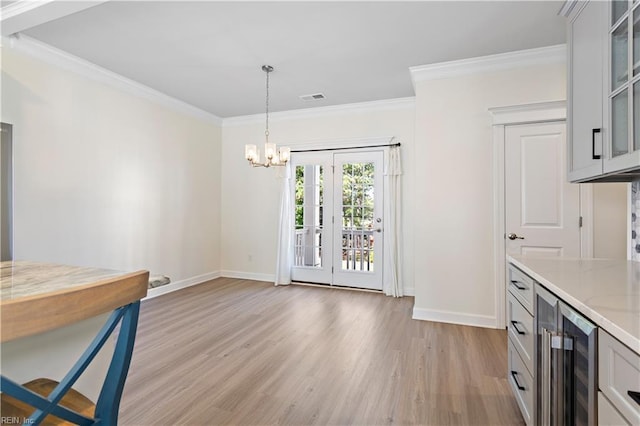 dining space with an inviting chandelier, crown molding, beverage cooler, and light wood-type flooring